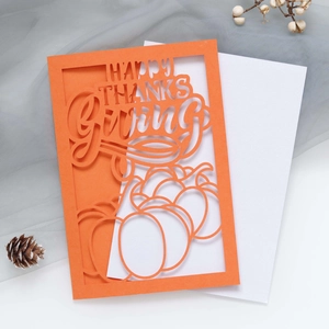 Macro detail of laser-cut orange Thanksgiving card with pumpkin motif and white envelope
