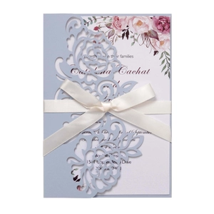 Detail of laser-cut floral light blue wedding invitation with a white satin ribbon bow