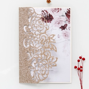 Detail of laser-cut gold glitter wedding invitation with floral sleeve and rose insert