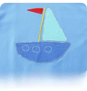 Dettaglio del ricamo a forma di barca a vela e scritta LA MER su maglietta azzurra
