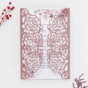 Close-up of laser cut rose gold glitter invitation with floral inner card for wedding