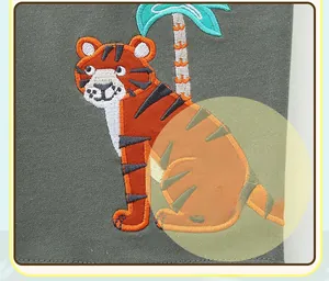Détail de broderie montrant un tigre et un palmier sur un tissu en coton vert foncé
