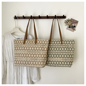 Detailed view of woven straw tote bags in beige and green geometric patterns on a wooden rack