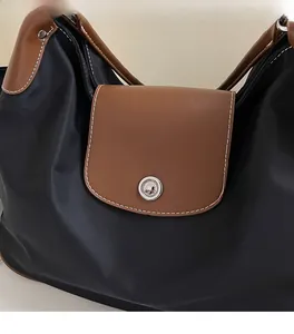 Close-up of black nylon tote bag with brown leather flap and contrast white stitching