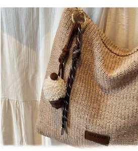 Dettaglio della borsa tote in paglia con ciondolo a cupcake e toppa in pelle del marchio