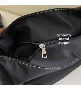 Detail of silver smooth metal zipper on black nylon tote bag with white stitching