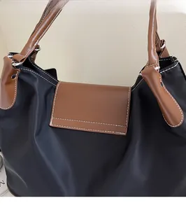 Detail showing white contrast stitching and brown leather handle on a black nylon tote bag