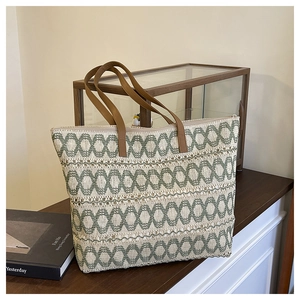 Detail of woven straw tote bag featuring green geometric patterns and brown leather straps