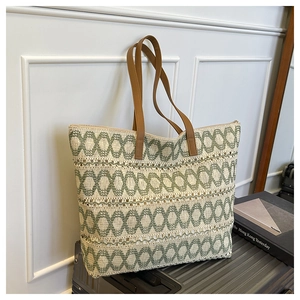 Detail of green geometric woven tote bag with brown leather handles on travel suitcase