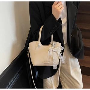 Détail du sac cabas crème en cuir grainé avec un pendentif nœud en dentelle et perles