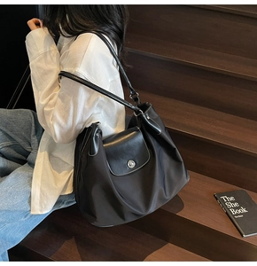 Detail view of black nylon tote bag featuring a leather flap and silver metal turn-lock closure
