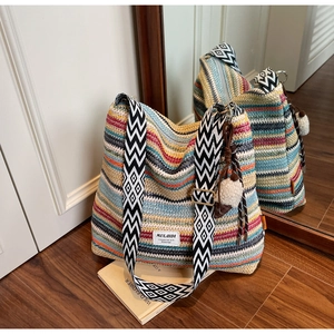 Detail of colorful woven bohemian beach bag with geometric strap and white pom pom charm