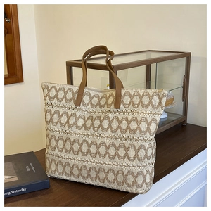 Detail of woven straw tote bag with geometric pattern and brown faux leather handles