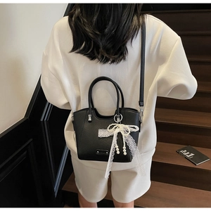 Détail du sac cabas en cuir noir avec nœud en dentelle et pendentif en perle élégant