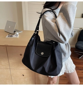 Detail of a large black tote bag with white contrast stitching and a metal twist lock pocket