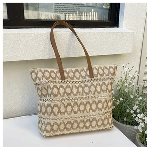 Detail of woven straw tote bag with brown leather handles against a white wall background