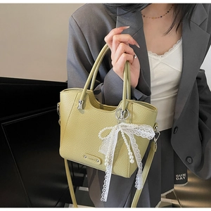 Détail du sac à main vert clair en cuir grainé avec pendentif en dentelle et logo métallique