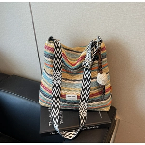 Detail of colorful striped woven beach bag with geometric strap and white pompom charm
