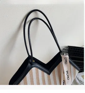 Detail showing striped woven tote texture with black leather handles and ribbon
