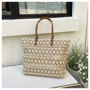 Detail of hand-woven straw tote with brown geometric wave pattern and leather handle