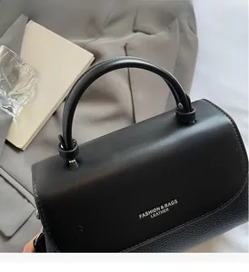 Detail of black pebbled leather handbag with curved handle and fashion branding