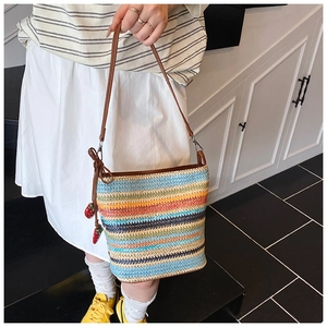 Detail of multi-color striped woven bucket bag with red strawberry charms and leather strap