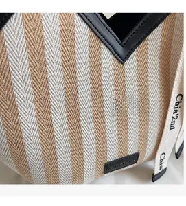 Detail of striped woven tote bag featuring black leather trim and branded shoulder strap