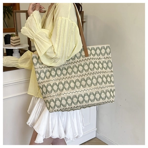 Detail of large woven tote bag featuring green geometric patterns and brown leather straps