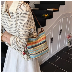 Detail of colorful striped woven shoulder bag with a strawberry charm on a female model