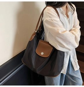 Detailed side view of black nylon tote bag with brown leather trim worn by model
