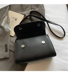 Close-up of black lychee leather bag showing dual magnetic closure and protective metal feet