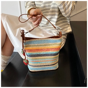 Close-up of handmade rainbow woven straw bucket bag with strawberry charms on a strap