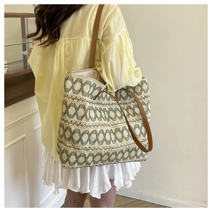 Detail view of woven straw tote bag featuring green wavy patterns and brown leather straps