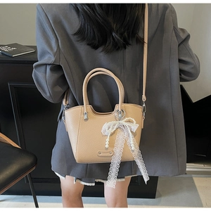 Détail du cabas en cuir beige avec nœud en dentelle et perles sur un mannequin