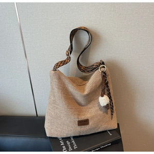 Close-up of woven straw bag with colorful geometric strap and plush ball charm detail