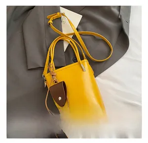 Detail of a yellow leather bucket bag with brown leaf charm on a grey blazer jacket