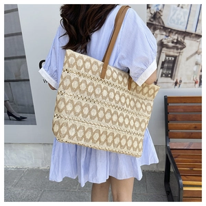 Detail of woven straw tote bag featuring brown diamond patterns and leather shoulder straps