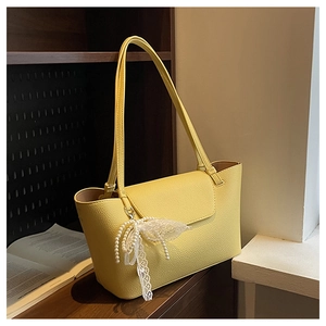 Detail of yellow tote bag with textured leather and a white lace pearl bow accessory