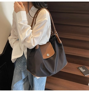 Detail of nylon tote bag with brown leather handles and flap against a wooden background