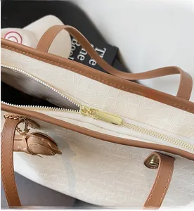 Detail of smooth gold zipper closure on off-white crocodile embossed tote bag