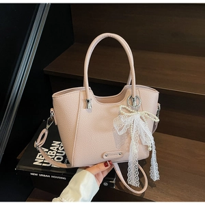 Détail du sac cabas en cuir grainé rose clair avec noeud en dentelle et perles sur escalier