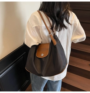 Detail of a large nylon tote bag with leather straps and metal lock worn by a model