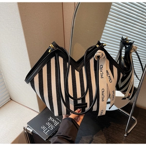 Detail view of M-shaped striped canvas bag with leather trim and woven lettering strap