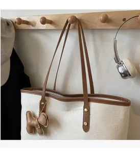 Close-up of white embossed tote bag with brown straps and cute puppy pendant accessory
