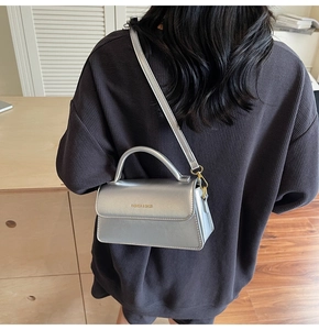 Detail of silver metallic crossbody bag showing gold fashion lettering and handle texture