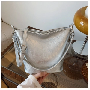 Detail der silbernen Metallic-Eimertasche mit Logogravur und verstellbarem Schultergurt