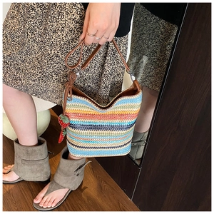Detail of colorful striped woven bucket bag featuring a strawberry charm and leather strap