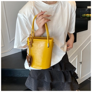 Detail of a bright yellow glossy bucket bag with brown leaf charm and sleek handles