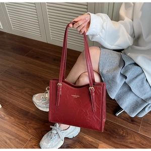 Detailed view of the dark red embossed leather texture and gold buckle on the tote bag