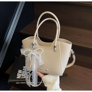 Détail du sac cabas beige motif litchi avec nœud en perles et breloque en dentelle